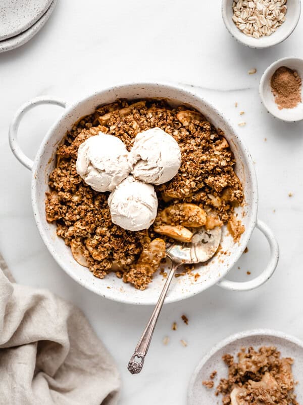apple crisp in a baking dish topped with three scoops of vanilla ice cream
