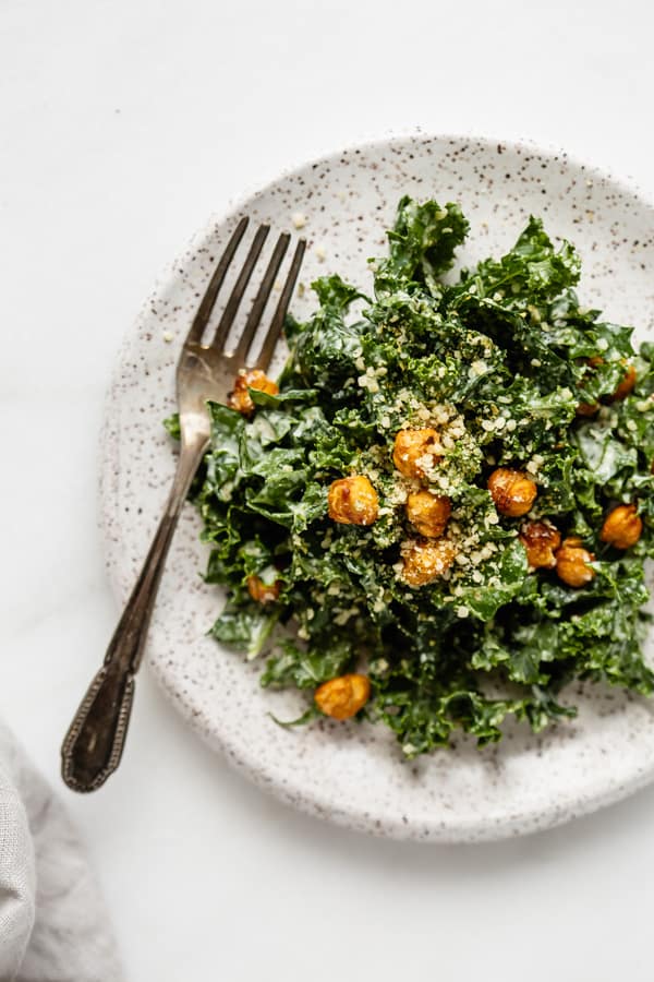 a speckled white plate with kale caesar salad and a small fork
