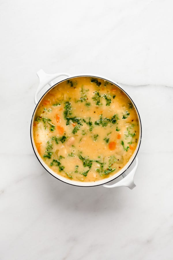 A white pot filled with tuscan white bean soup on a marble board