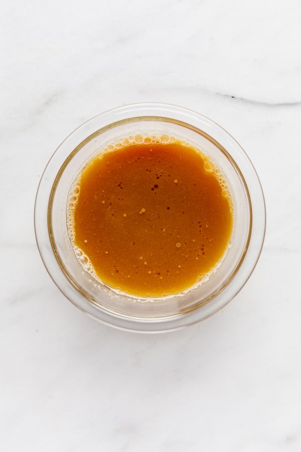 a clear mixing bowl with apple cider and oil in it