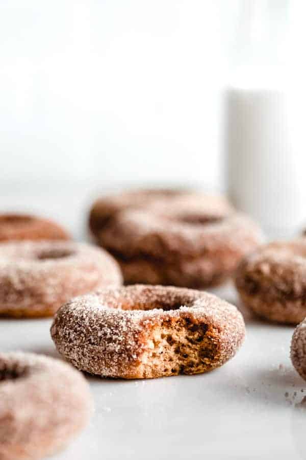 A vegan apple cider donut covered in cinnamon sugar with a bite taken out of it