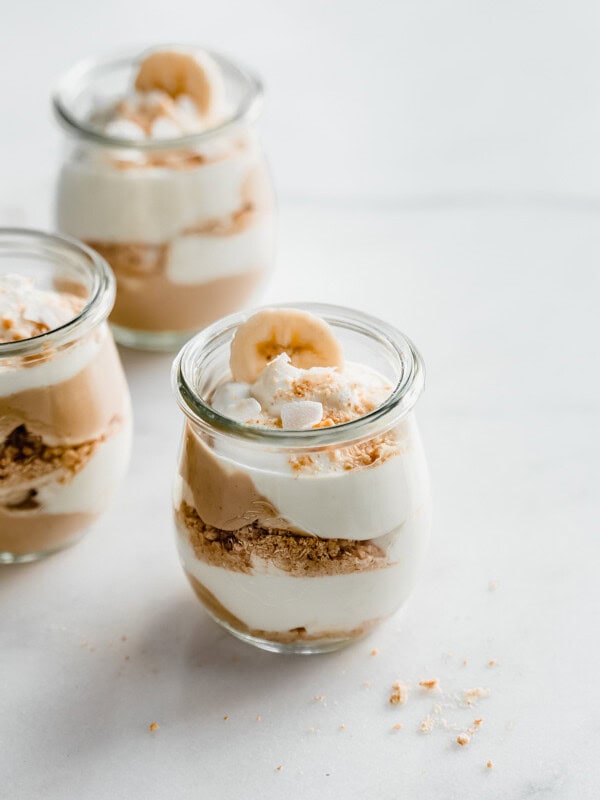 a cup of banana cream pie parfait with layers of pudding, coconut whipped cream, graham cracker crumbs and banana