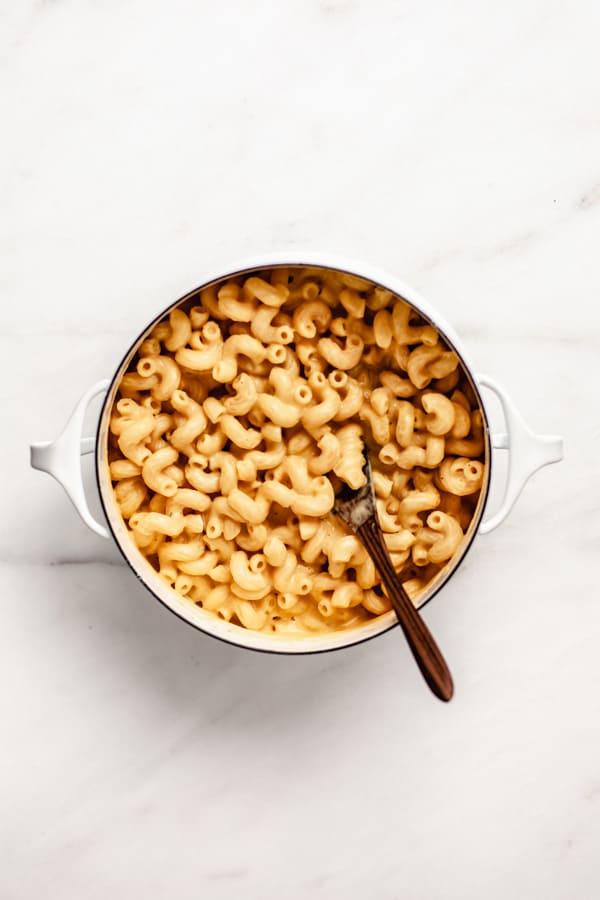 a white pot filled with butternut squash mac and cheese with a wooden mixing spoon in it