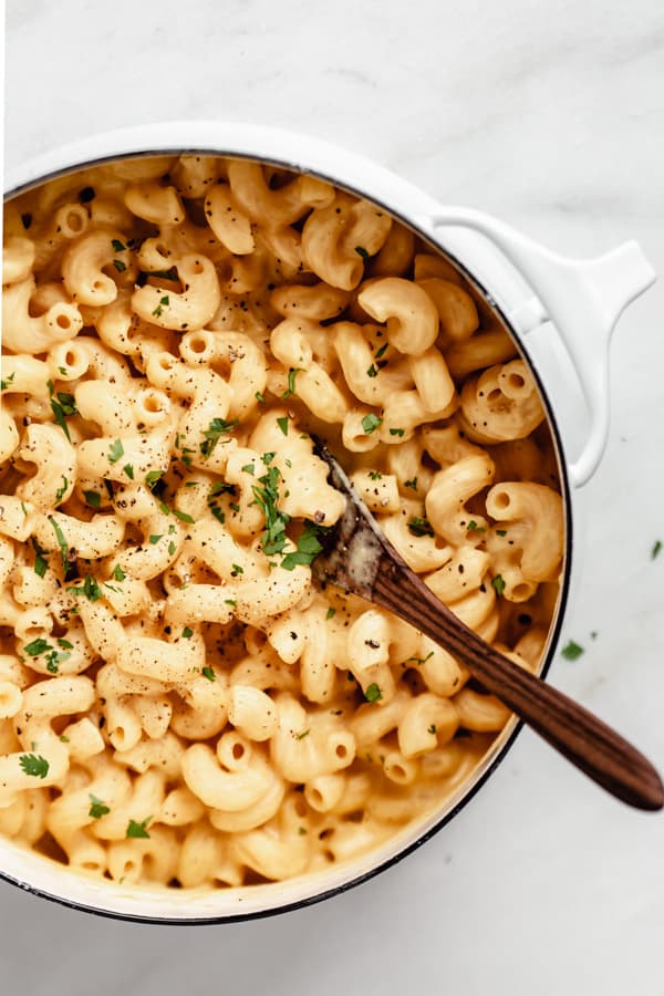 a white pot filled with butternut squash mac and cheese topped with pepper and chopped parsley