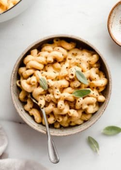 A ceramic bowl filled with butternut squash mac and cheese topped with sage leaves