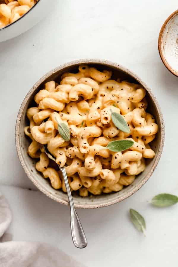 A ceramic bowl filled with butternut squash mac and cheese topped with sage leaves