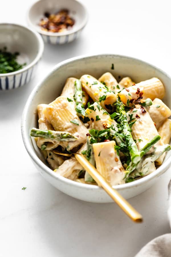 creamy rigatoni pasta in a white bowl with a gold fork