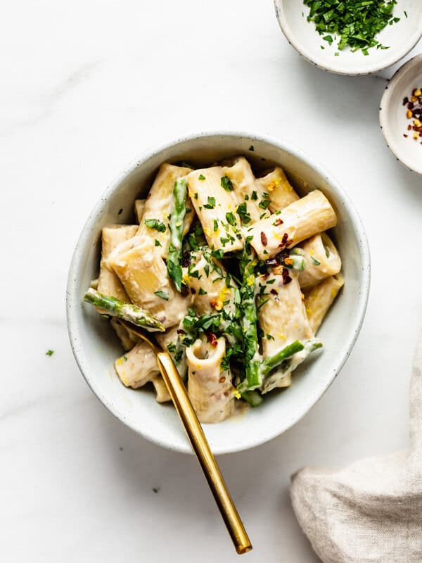 A bowl of rigatoni with asparagus and a gold fork in it