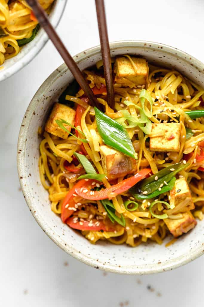 a bowl of singapore noodles with sliced green onions and sesame seeds on top