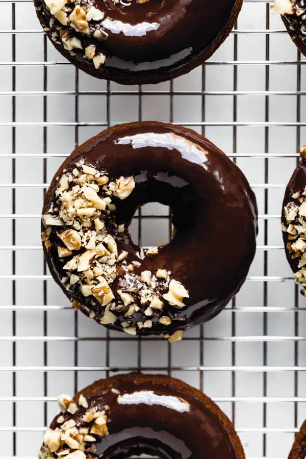 a close up of a donut topped with chocolate glaze and crushed walnuts on a silver cooling rack