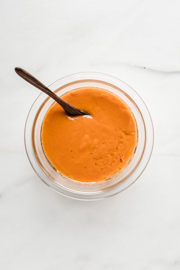 a clear mixing bowl with pumpkin puree and a wooden spoon in it