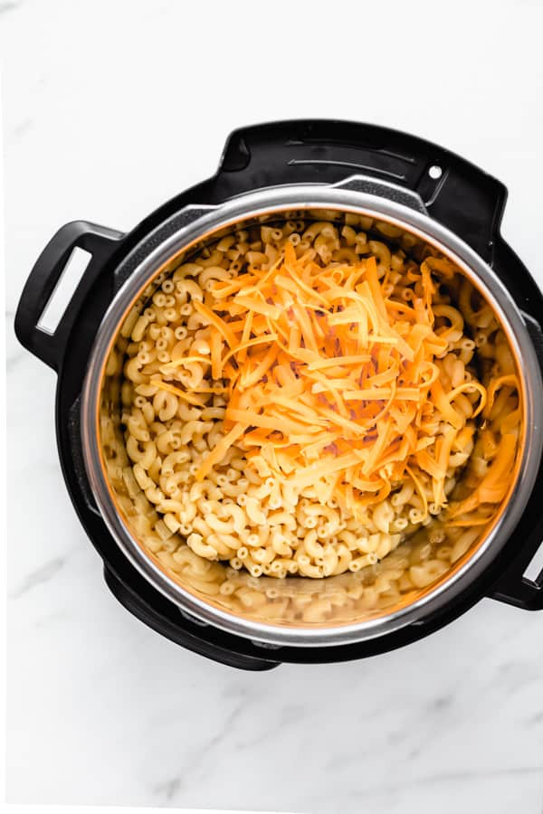 macaroni in an instant pot with a pile of orange shredded cheese on it