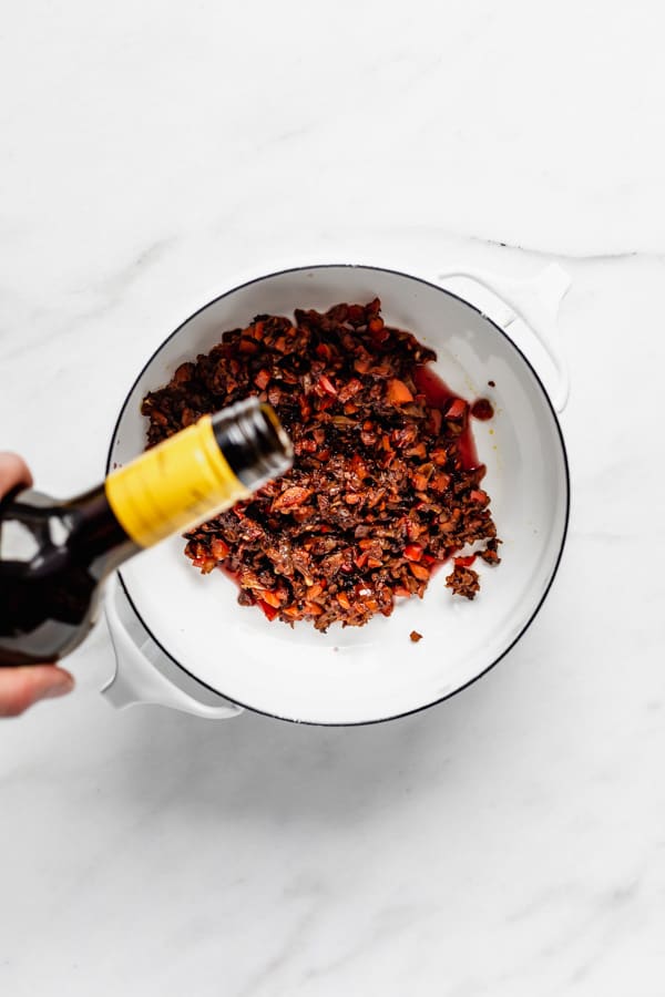 a hand pouring red wine into a white pot filled with vegetables