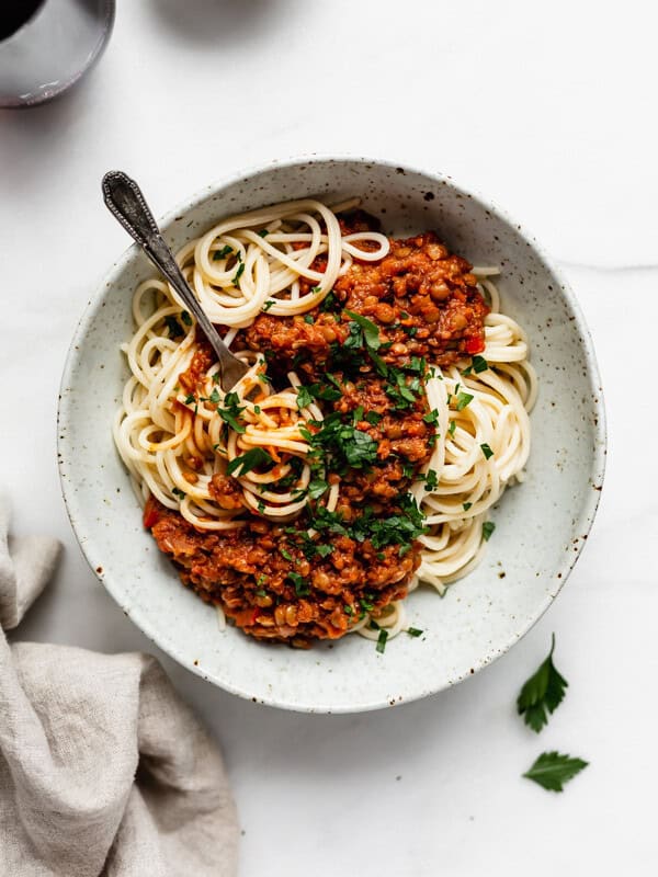 spaghetti with lentil bolognese in a white speckeld pasta bowl and a napkin on the side