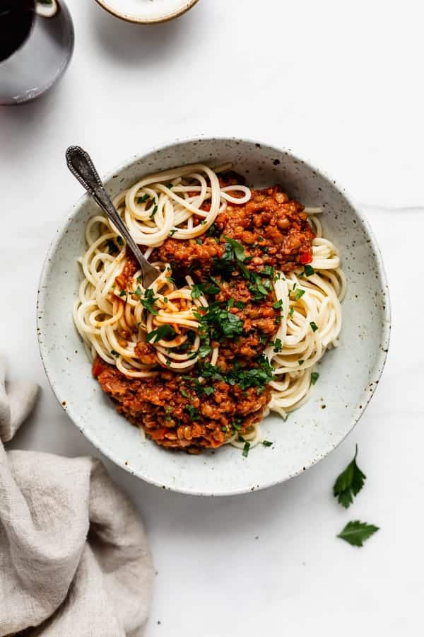 spaghetti with lentil bolognese in a white speckeld pasta bowl and a napkin on the side