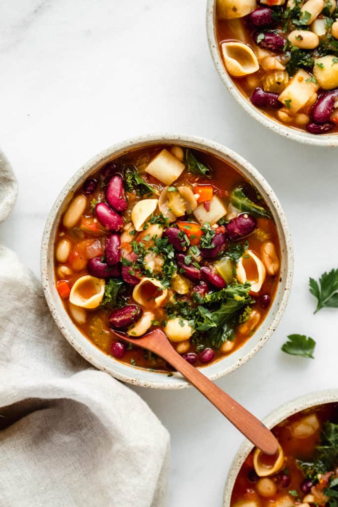 three bowls of vegan minestrone soup with a linen napkin on the side