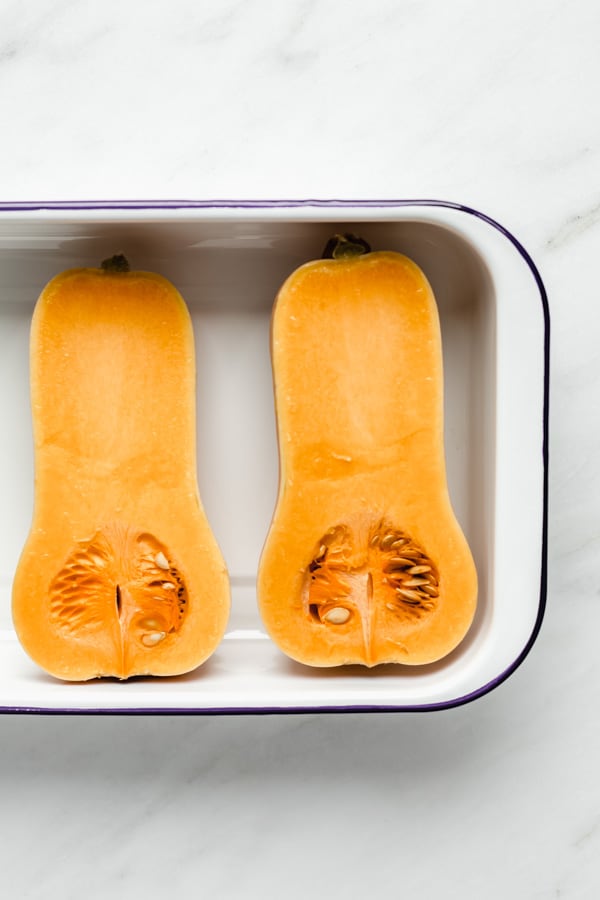 two halves of butternut squash in a white roasting pan