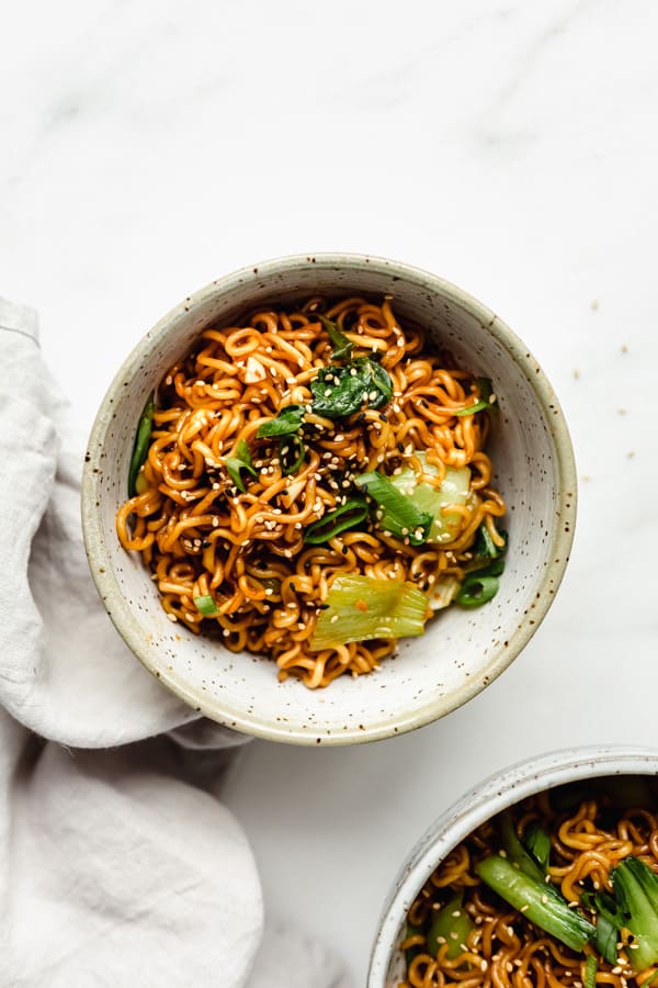 two bowls of ramen noodles topped with green onions and sesame seeds
