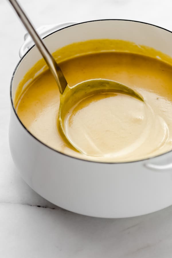 a ladle scooping up a spoonful of cauliflower soup from a white pot