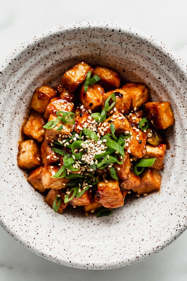 A bowl of General Tso Tofu topped with green onions and sesame seeds
