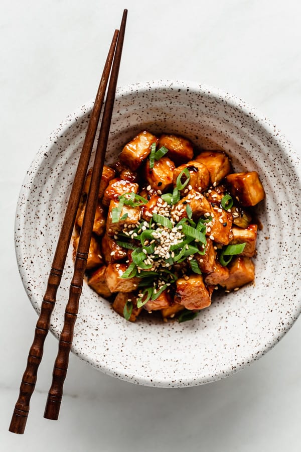 General Tso Tofu in a white speckled bowl with chopsticks on the side