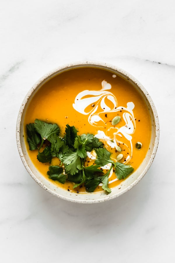 a bowl of butternut squash soup topped with cilantro, coconut milk and pumpkin seeds