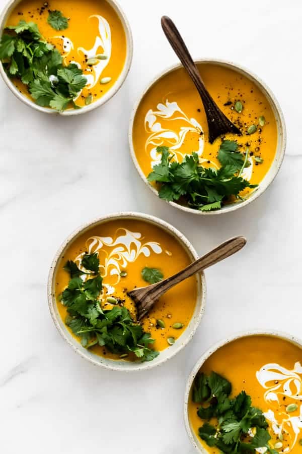 four bowl of butternut squash soup with wooden spoons in them