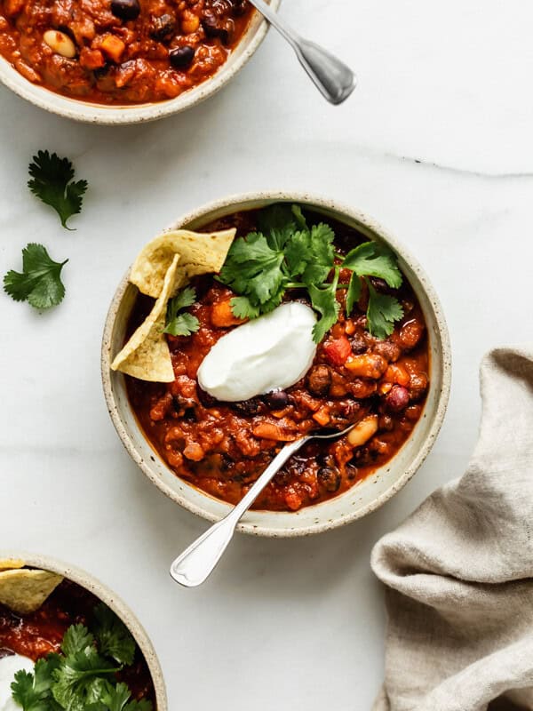 three bowls of vegan chili topped with vegan sour creme, cilantro and tortilla chips