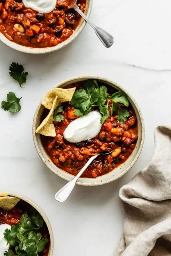 three bowls of vegan chili topped with vegan sour creme, cilantro and tortilla chips