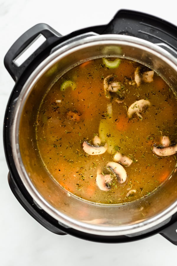 an instant pot with broth and veggies in it