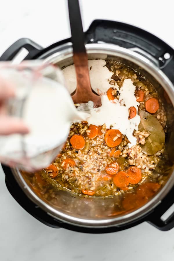 a measuring cup pouring cashew cream into an instant pot of wild rice soup