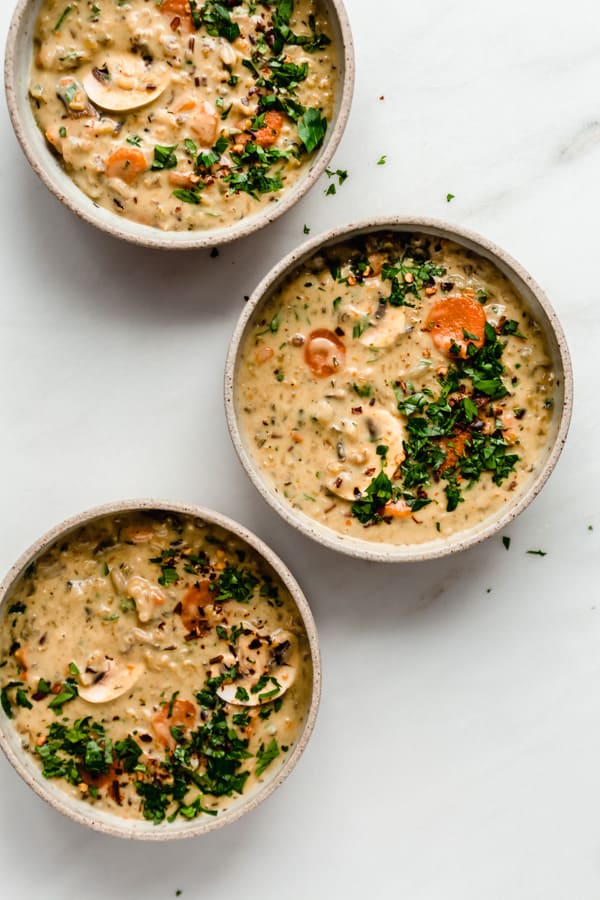 three bowls of wild rice soup topped with parsley