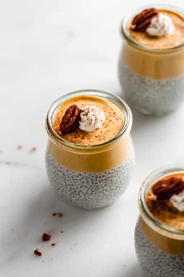 a small jar of pumpkin pie chia pudding topped with whipped cream and a pecan