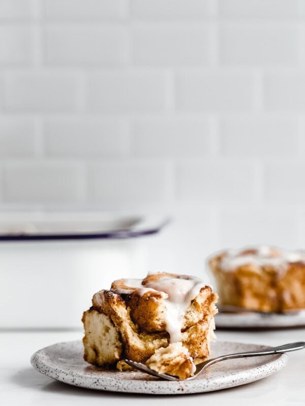 a cinnamon roll on a plate with a white pan in the background