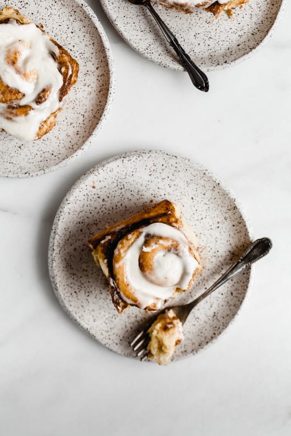 three white speckeld plates with cinnamon rolls on them