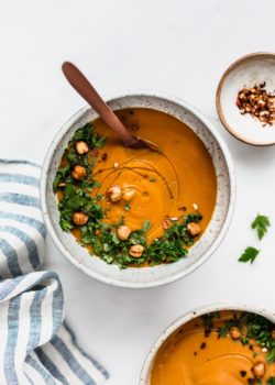 a bowl of sweet potato soup with a striped napkin on the side and a small dish of chilli flakes