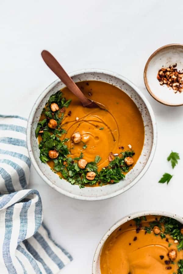 a bowl of sweet potato soup with a striped napkin on the side and a small dish of chilli flakes
