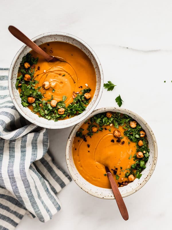 two bowls of sweet potato soup with wooden spoons in them