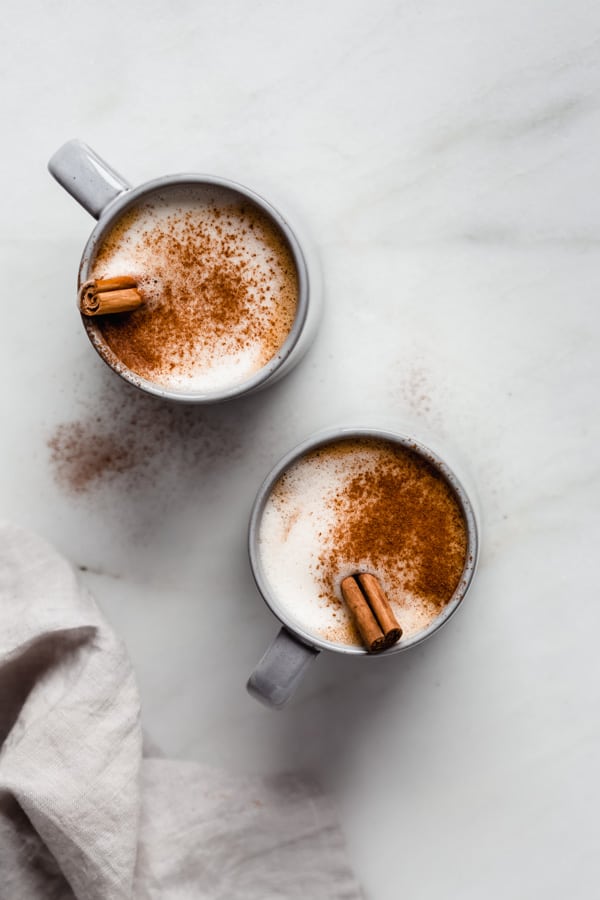 two blue mugs of pumpkin spice latte with cinnamon sticks in them