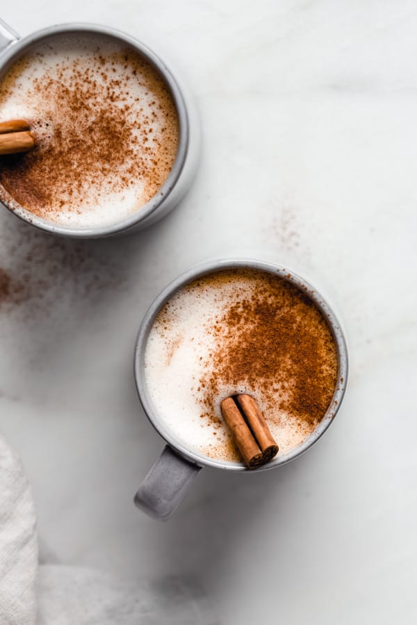 two blue mugs of pumpkin spice latte with cinnamon and cinnamon sticks on top
