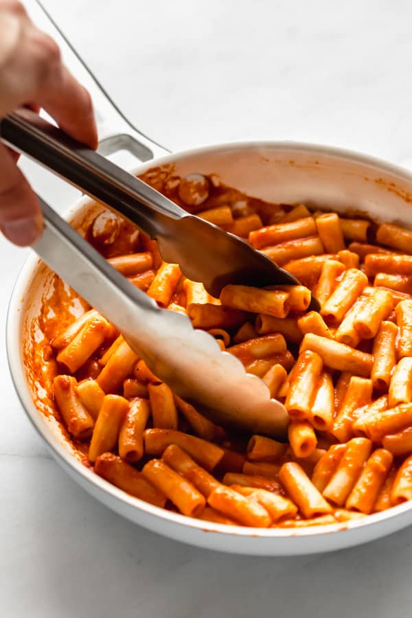 tongs scooping up roasted red pepper pasta from a pan