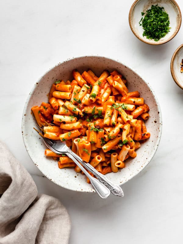roasted red pepper pasta in a white speckled pasta bowl with a side of parsley