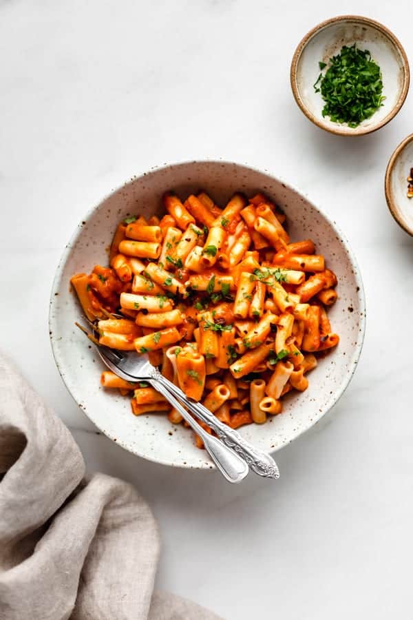 roasted red pepper pasta in a white speckled pasta bowl with a side of parsley