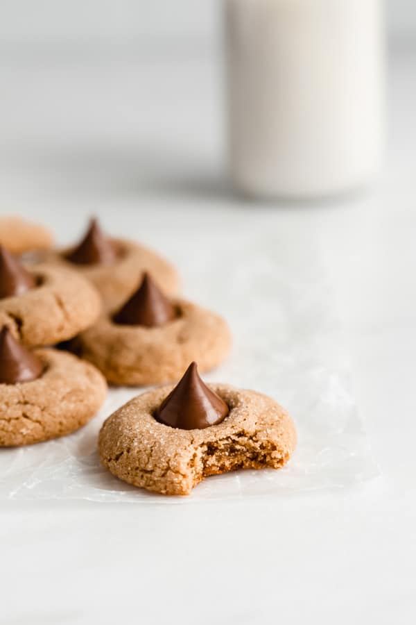 peanut butter blossom cookies on parchment paper with a jug of milk in the back