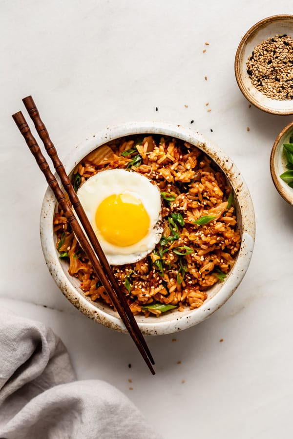 Kimchi fried rice in a white bowl topped with an egg and sesame seeds in a small bowl on the side