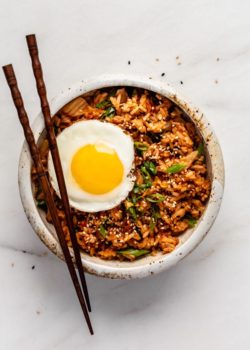 A bowl of kimchi fried rice topped with an egg and chopsticks on top