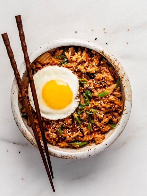 A bowl of kimchi fried rice topped with an egg and chopsticks on top