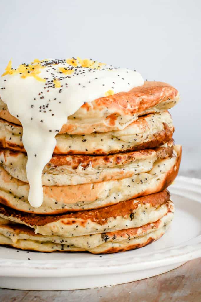 healthy breakfast plate of lemon poppyseed pancakes topped with white yogurt, poppyseeds, and lemon zest