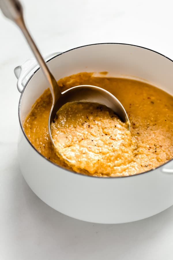 a ladle scooping up red lentil dal out of a white pot