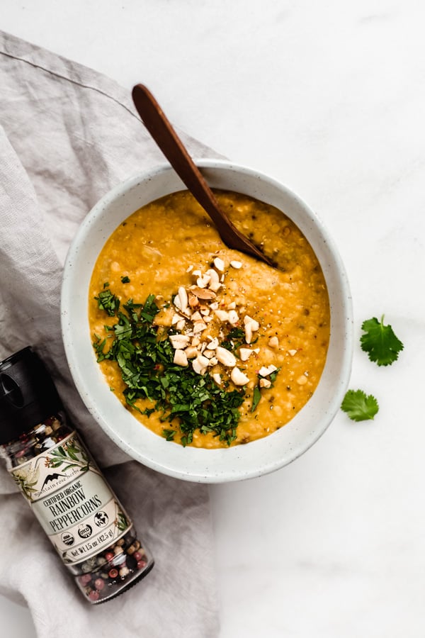 A bowl of red lentil dal with rainbow peppercorn grinder next to it